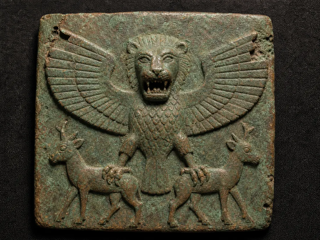 Copper-coloured votive plaque of a frontal eagle with a lion's head, wings spread wide, each talon gripping a stag by the back