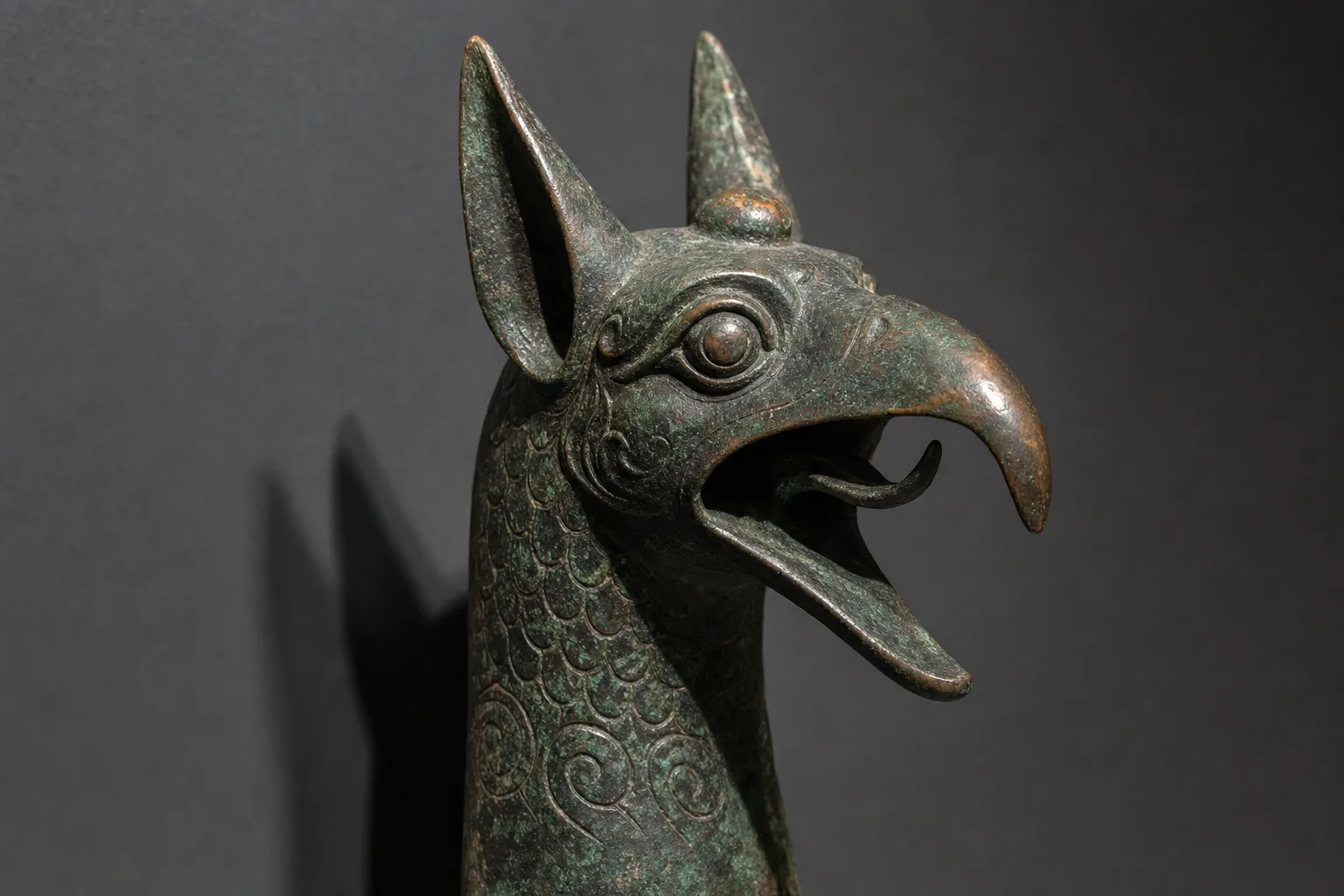 Cast bronze griffin head with open beak, upright ears and a knob on the forehead, green with age